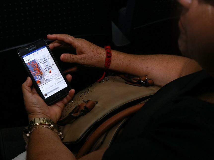 No celular, Maria* compartilha mensagens de fé para renovar a esperança à espera do filho. (Foto: Henrique Kawaminami)